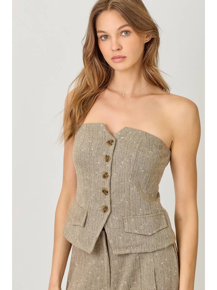 Woman wearing a beige strapless outfit with button details on a plain background